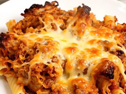A close-up of cheesy baked ziti in a slow cooker with visible melty ricotta and rich marinara sauce.