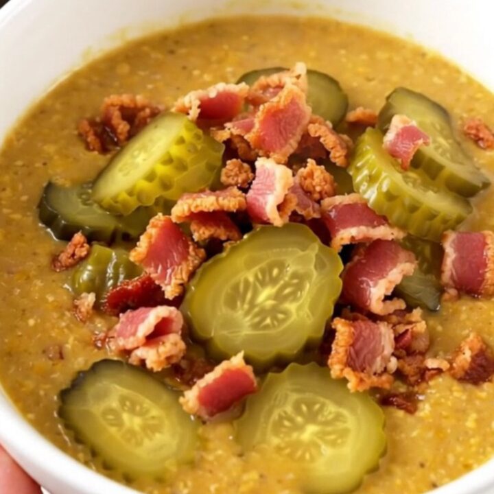 A steaming bowl of creamy cheeseburger soup topped with crispy bacon and diced pickles.