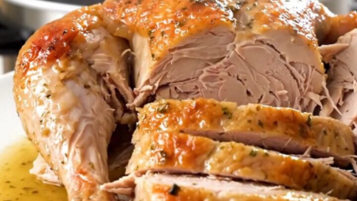 A beautifully cooked, glistening turkey breast seasoned with fresh rosemary on a white plate.