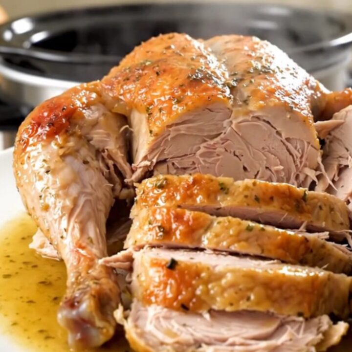 A beautifully cooked, glistening turkey breast seasoned with fresh rosemary on a white plate.