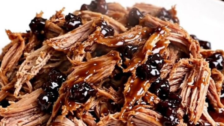 A slow cooker filled with tender pulled pork glazed in a rich blackberry sauce with visible pieces of jalapeno.