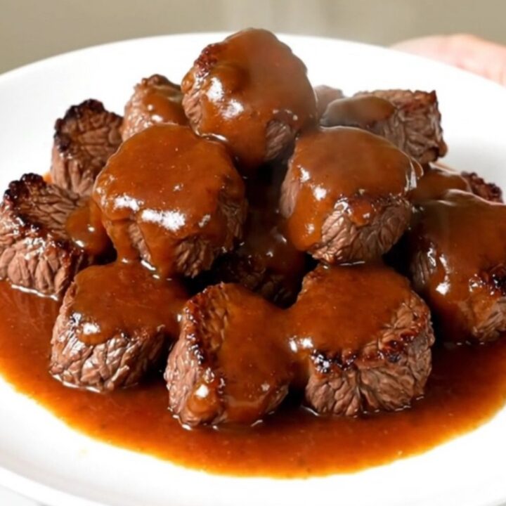 A top-down view of raw steak cubes, red bell peppers, and chili sauce being added to a slow cooker.