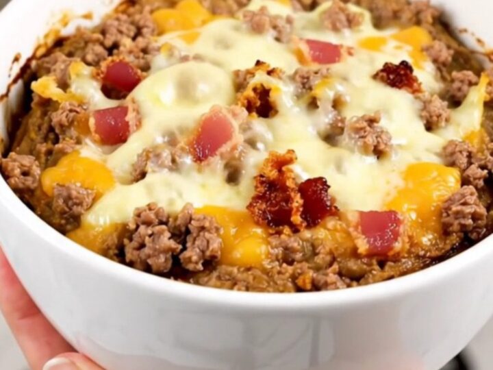 A top-down view of a black slow cooker filled with a creamy bacon double cheeseburger dip on a white quartz countertop.
