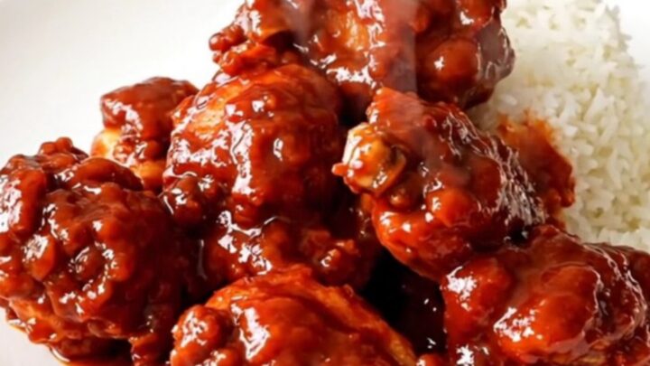 A close-up of glossy firecracker chicken served over white rice on a white plate.