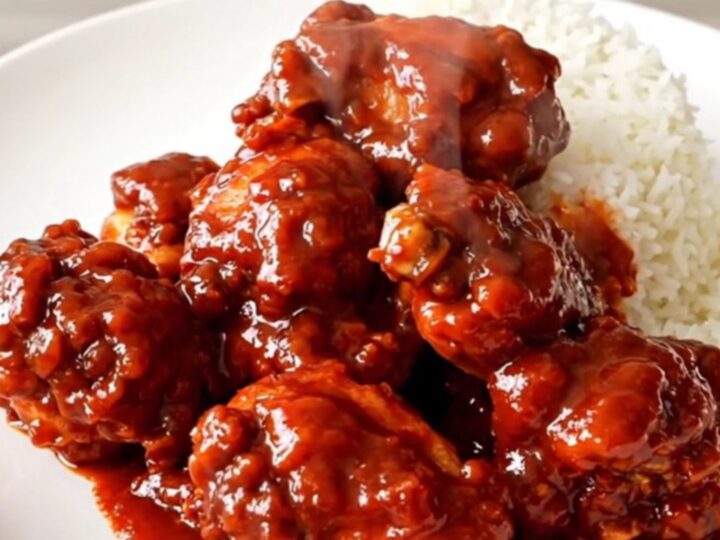 A close-up of glossy firecracker chicken served over white rice on a white plate.
