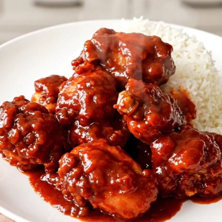 A close-up of glossy firecracker chicken served over white rice on a white plate.