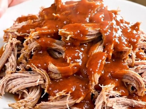 A close-up of a slow cooker filled with shredded buffalo ranch pork on a white speckled countertop.