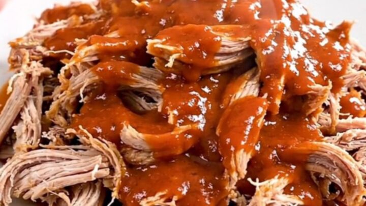 A close-up of a slow cooker filled with shredded buffalo ranch pork on a white speckled countertop.