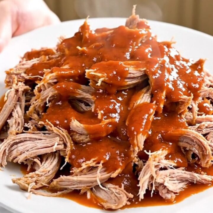 A close-up of a slow cooker filled with shredded buffalo ranch pork on a white speckled countertop.