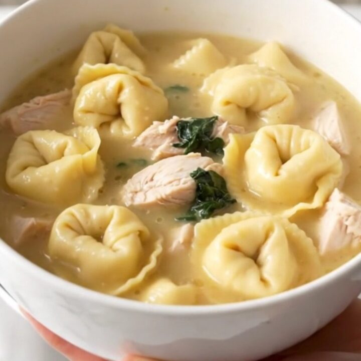 A steaming bowl of creamy chicken tortellini soup with visible pieces of chicken and fresh spinach.