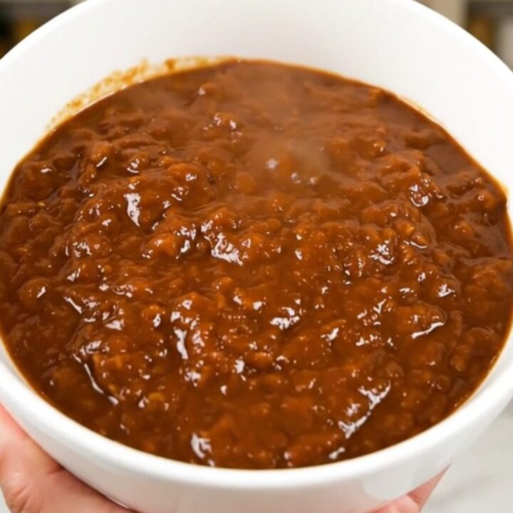 A top-down view of a black slow cooker filled with hearty beef and kidney bean chili.