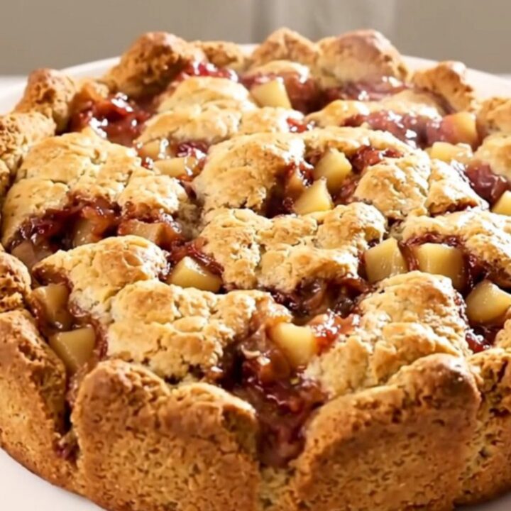 A warm, golden-crusted apple cobbler inside a black slow cooker insert on a white countertop.