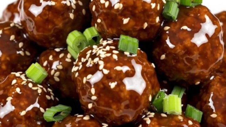 A plate of glossy, steaming General Tso meatballs served on a white round plate with a soft blurred kitchen background.