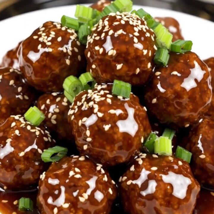 A plate of glossy, steaming General Tso meatballs served on a white round plate with a soft blurred kitchen background.