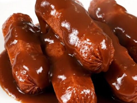 Glossy, dark barbecue-glazed cocktail smokies piled on a white plate.
