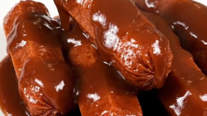 Glossy, dark barbecue-glazed cocktail smokies piled on a white plate.