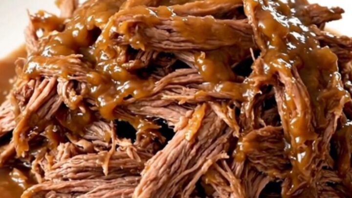 A close-up of a tender, shredded pot roast served on a white plate with a glossy apple butter glaze.