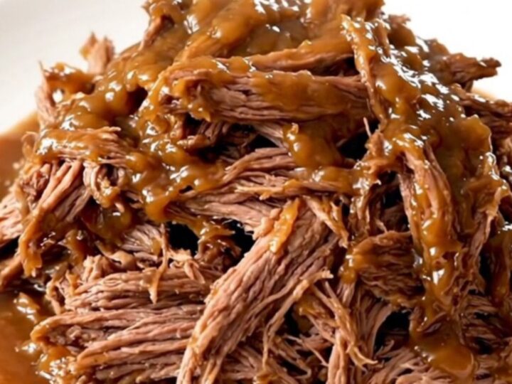 A close-up of a tender, shredded pot roast served on a white plate with a glossy apple butter glaze.