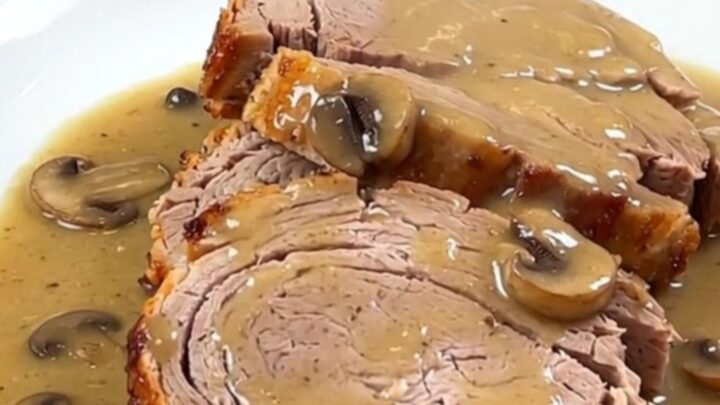 A close-up of a tender sliced pork loin smothered in a rich, glossy creamy mushroom gravy on a white plate.
