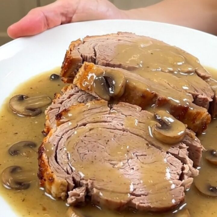 A close-up of a tender sliced pork loin smothered in a rich, glossy creamy mushroom gravy on a white plate.