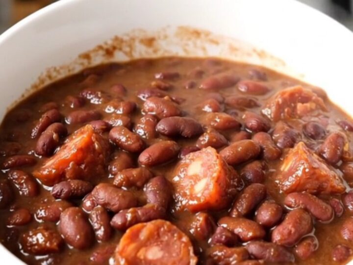 A slow cooker filled with hearty charro beans, chorizo, and onions on a white quartz countertop.