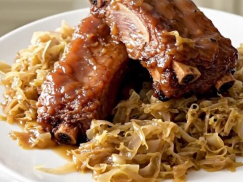 A close-up of slow-cooked country-style pork ribs covered in a shiny glaze and tangy sauerkraut.