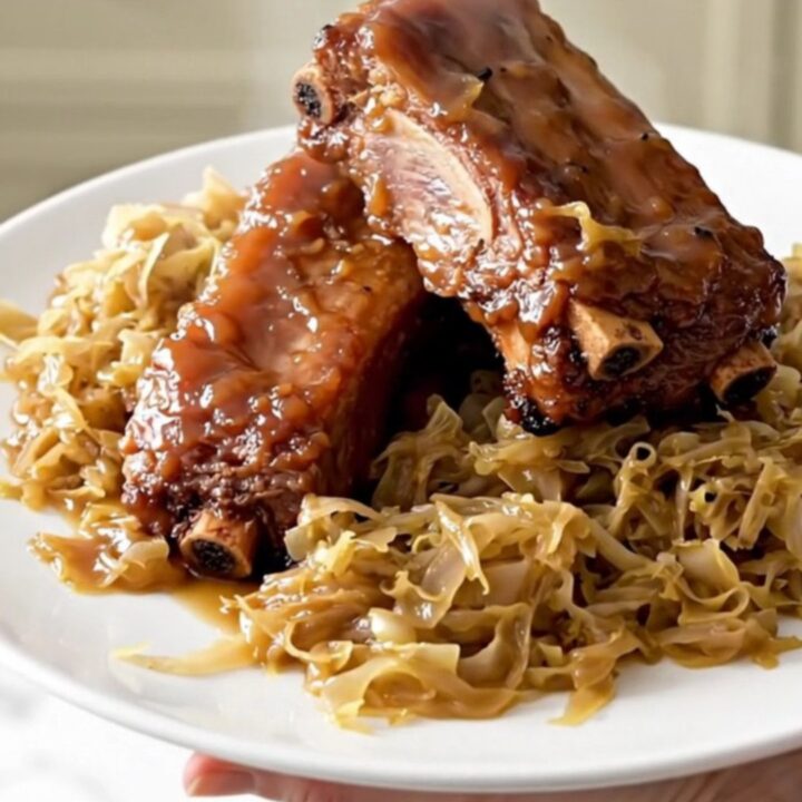 A close-up of slow-cooked country-style pork ribs covered in a shiny glaze and tangy sauerkraut.