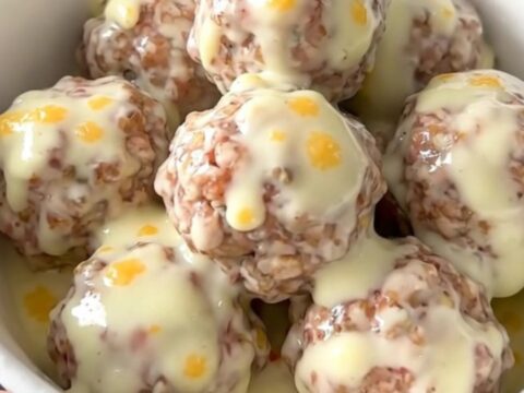 A white bowl filled with creamy queso blanco meatballs garnished with green chiles.