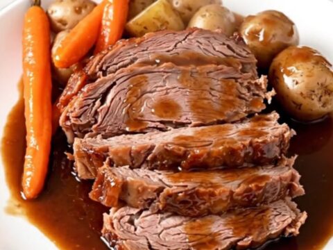 A rustic platter featuring tender sliced beef chuck roast surrounded by glazed red potatoes and soft carrots.