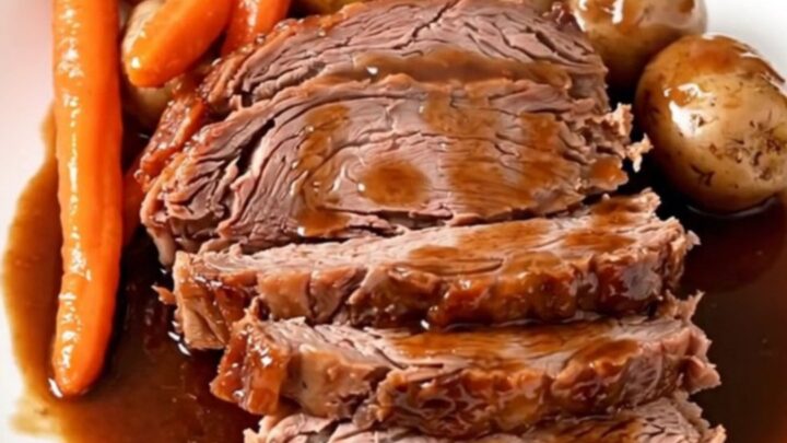 A rustic platter featuring tender sliced beef chuck roast surrounded by glazed red potatoes and soft carrots.