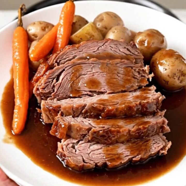 A rustic platter featuring tender sliced beef chuck roast surrounded by glazed red potatoes and soft carrots.