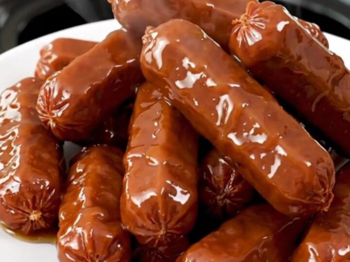 A black slow cooker on a white countertop filled with glazed maple bacon cocktail smokies.