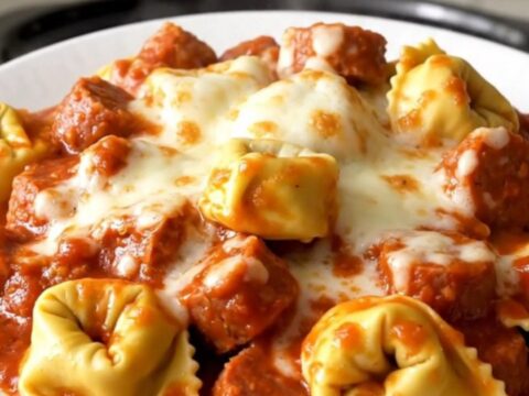A close-up of a bowl of slow-cooked Italian sausage and cheese tortellini topped with melted mozzarella.