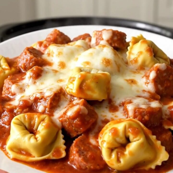 A close-up of a bowl of slow-cooked Italian sausage and cheese tortellini topped with melted mozzarella.
