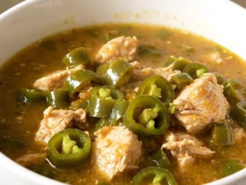 A white bowl filled with steaming green chile chicken stew on a quartz countertop.