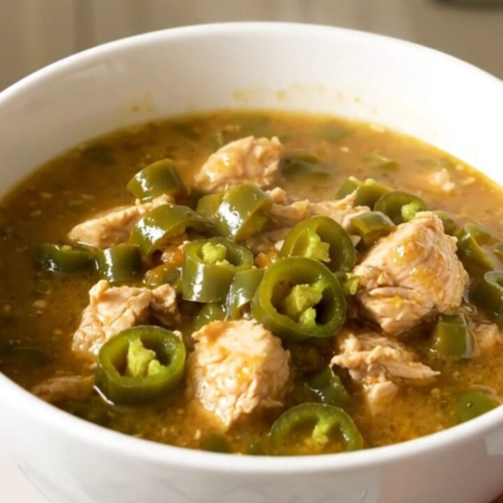 A white bowl filled with steaming green chile chicken stew on a quartz countertop.