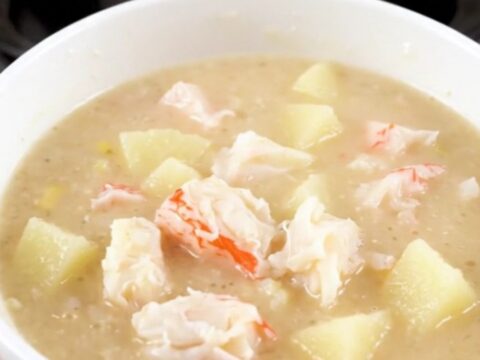A steaming bowl of creamy crab chowder with visible pieces of potato and crab meat.