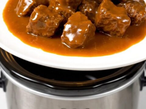 A close-up of tender orange beef strips served on a white plate with a glossy, vibrant sauce.