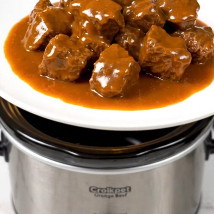 A close-up of tender orange beef strips served on a white plate with a glossy, vibrant sauce.