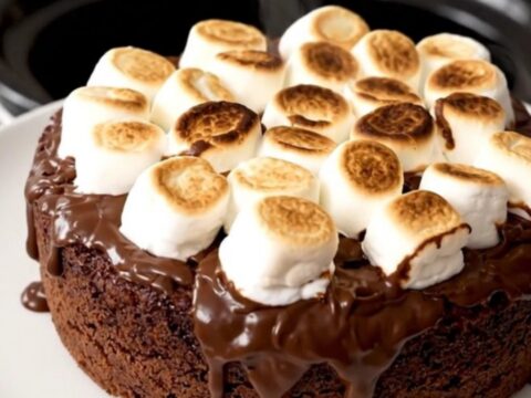 A top-down view of a black slow cooker filled with a freshly prepared chocolate s'mores dump cake.