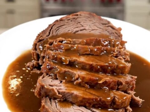 A close-up of a tender, sliced pot roast with glossy horseradish gravy on a white plate.