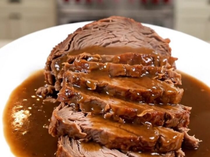 A close-up of a tender, sliced pot roast with glossy horseradish gravy on a white plate.