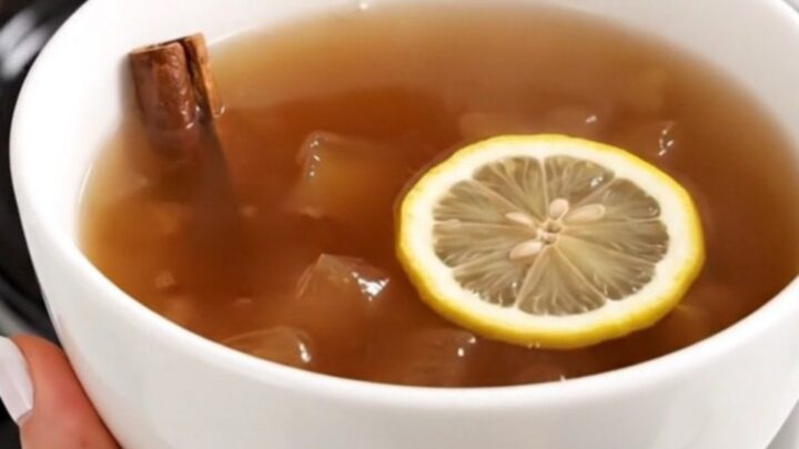 A steaming, glossy apple cider served in a plain white ceramic bowl against a blurred kitchen background.