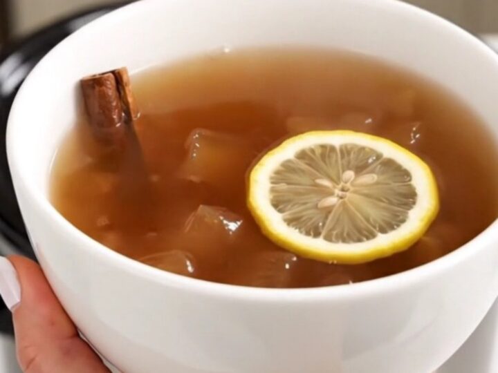 A steaming, glossy apple cider served in a plain white ceramic bowl against a blurred kitchen background.