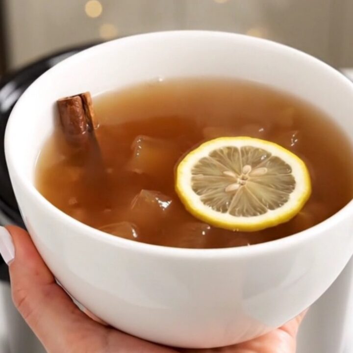 A steaming, glossy apple cider served in a plain white ceramic bowl against a blurred kitchen background.