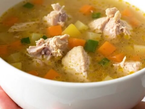 A steaming bowl of chicken vegetable soup with carrots and corn in a clear broth.
