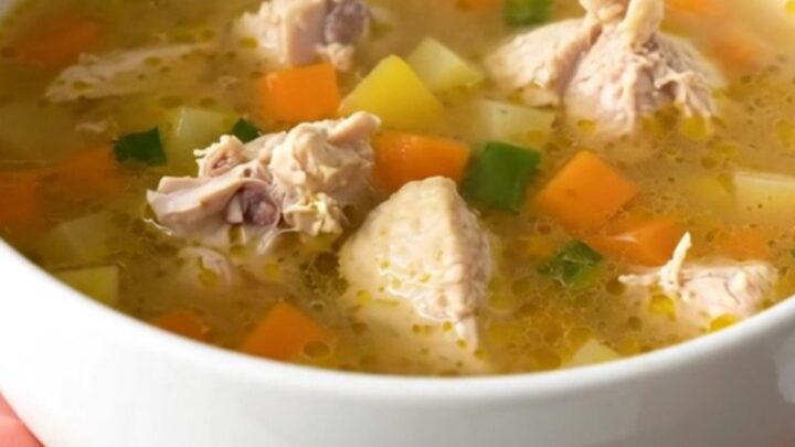 A steaming bowl of chicken vegetable soup with carrots and corn in a clear broth.