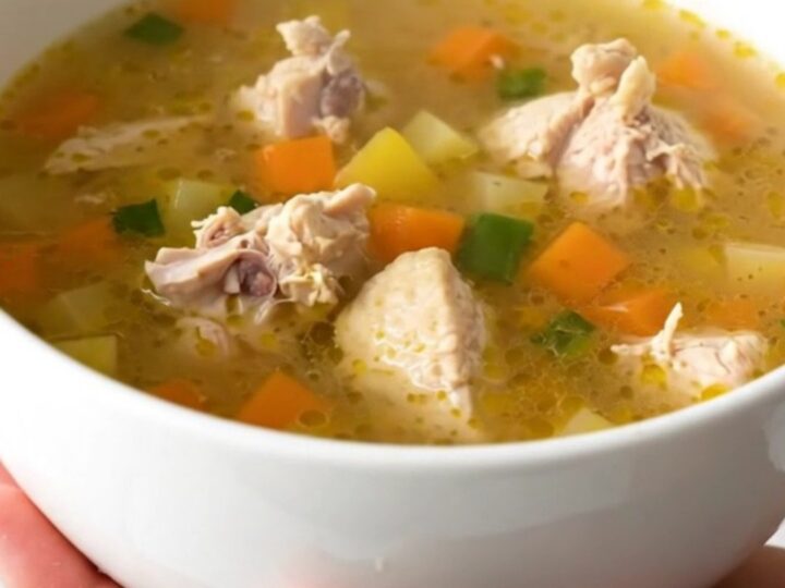 A steaming bowl of chicken vegetable soup with carrots and corn in a clear broth.