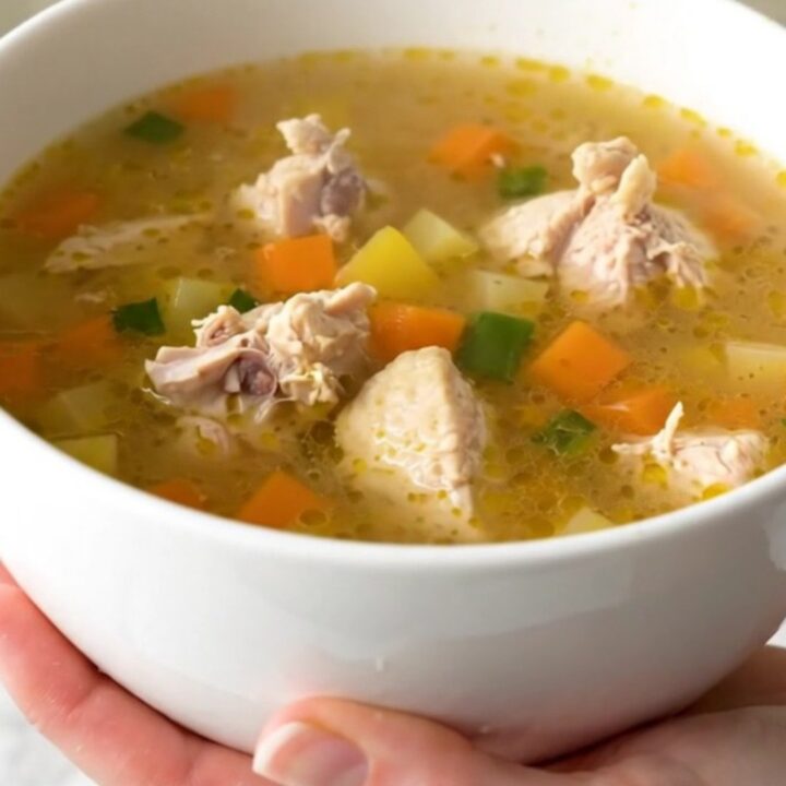 A steaming bowl of chicken vegetable soup with carrots and corn in a clear broth.