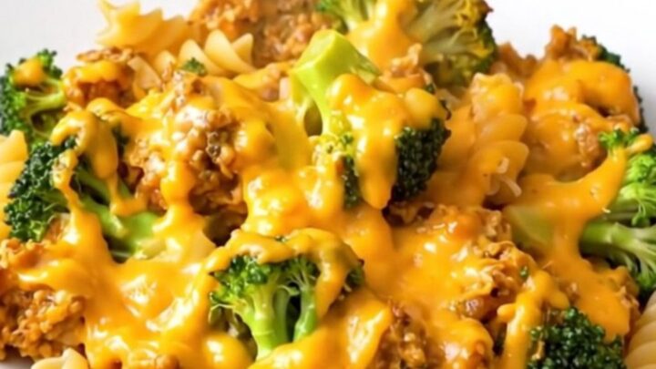 A steaming bowl of rotini pasta with broccoli florets coated in a thick, creamy cheddar cheese sauce.